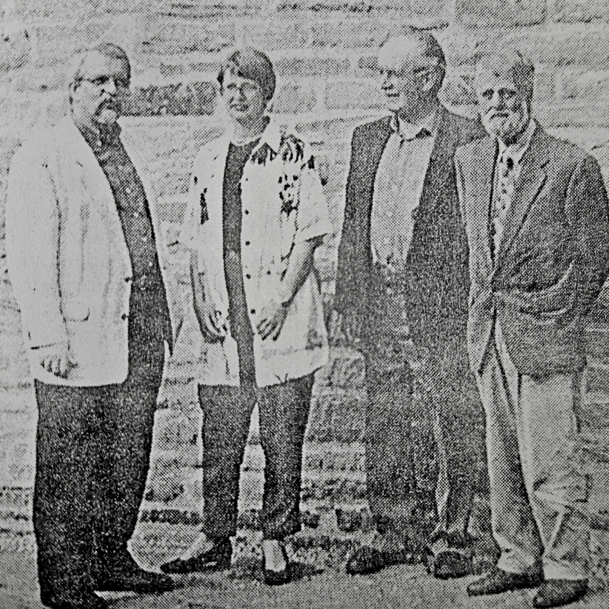 Ein schwarz-weißes Bild auf einer Zeitung zeigt drei Männer und eine Frau vor der Dorfkirche