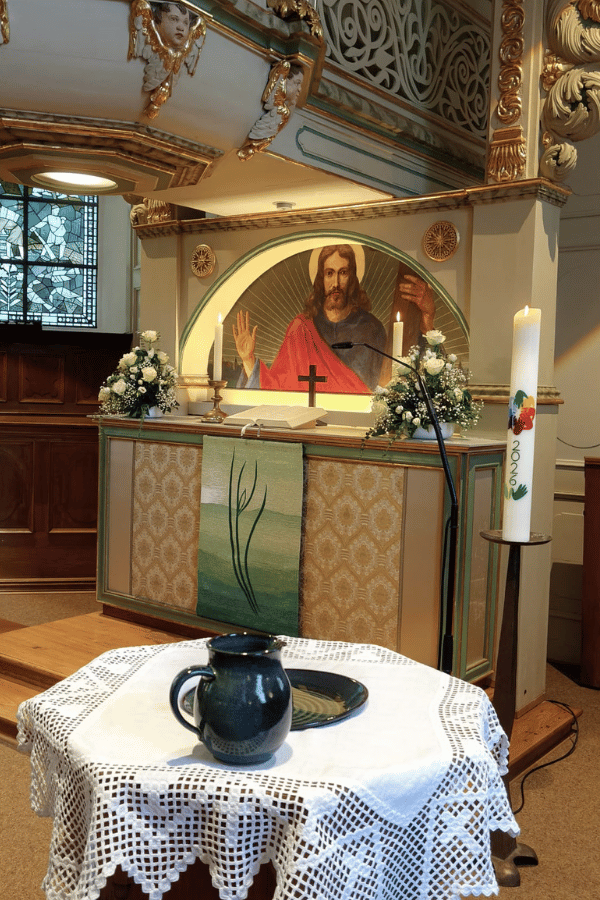 Die Aufnahme zeigt den Innenraum der Dorfkirche. Im Vordergrund ist der Taufstein zu sehen, dahinter der Altarraum.