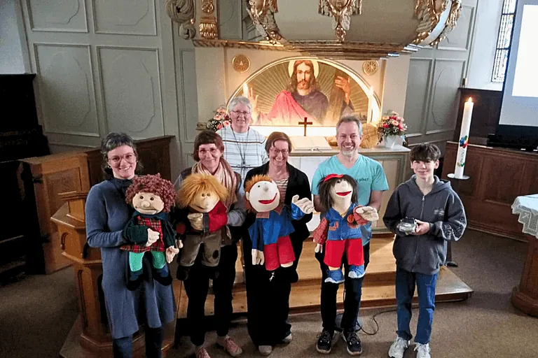 Das Team der Mini-Kirche. Sechs Personen stehen vor dem Altar der Dorfkirche. Vier Personen habe große Puppen im Arm. Mit den Puppen haben sie den Gottesdienst gestaltet. 