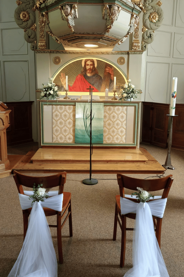 Aufnahme aus dem Innenraum der Dorfkirche. Vor dem Altar stehen zwei Stühle die mit weißem Stoff und weißen Blumen für eine Hochzeit geschmückt sind